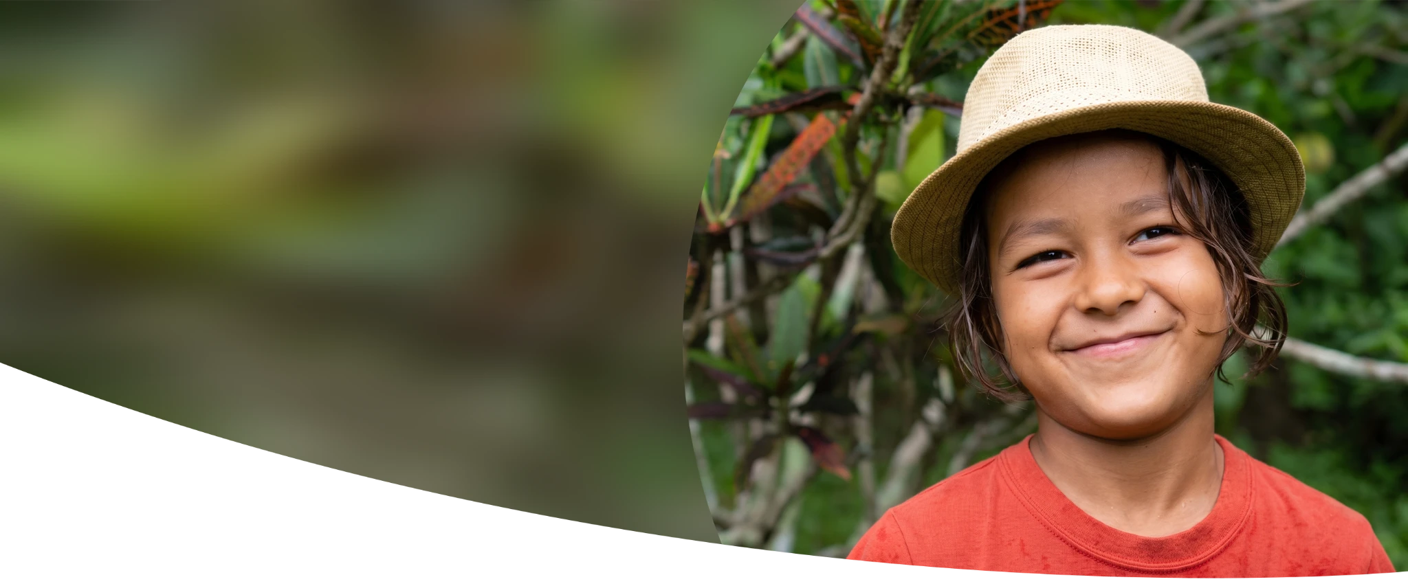 A smiling child wearing a straw hat in a garden